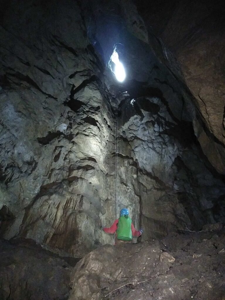 Un spéléologue est en bas d'un puits. En haut, il y a la lumière du jour.